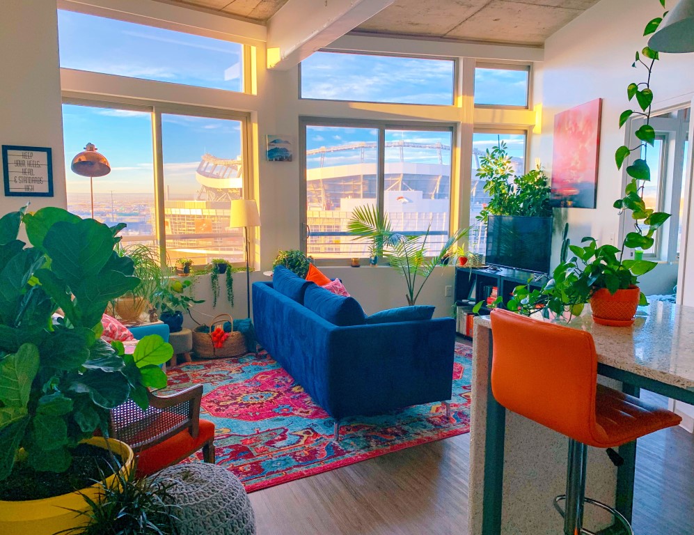 Maximalist Living Room With a bright blue sofa, rich deep red bar stool and tons of plants.